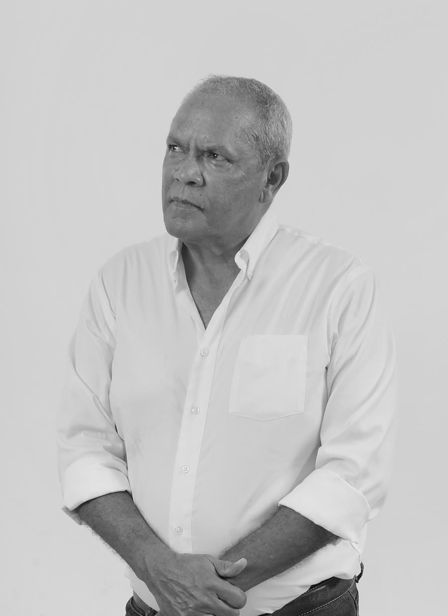 Black and white portrait of Drs. Mario Enrique Croes in a white shirt against a plain grey background